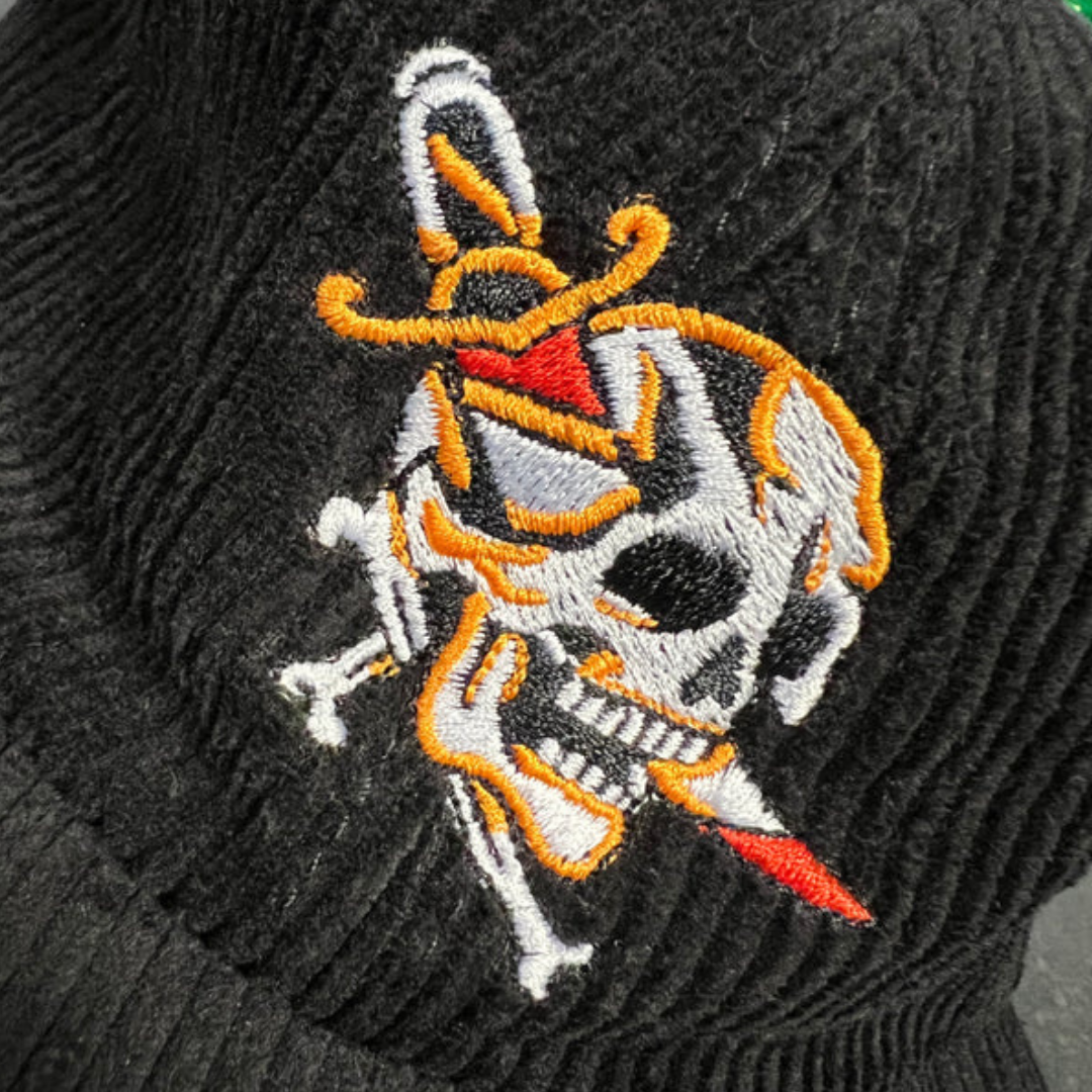 Dagger skull cord cap in black, close up image highlighting the embroidered traditional tattoo style skull with a dagger through the cheek