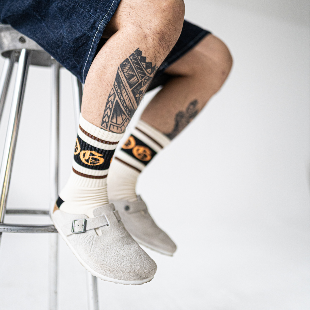 White OG socks with two espresso stripes and a black band with an orange OG logo worn by a tattooed model