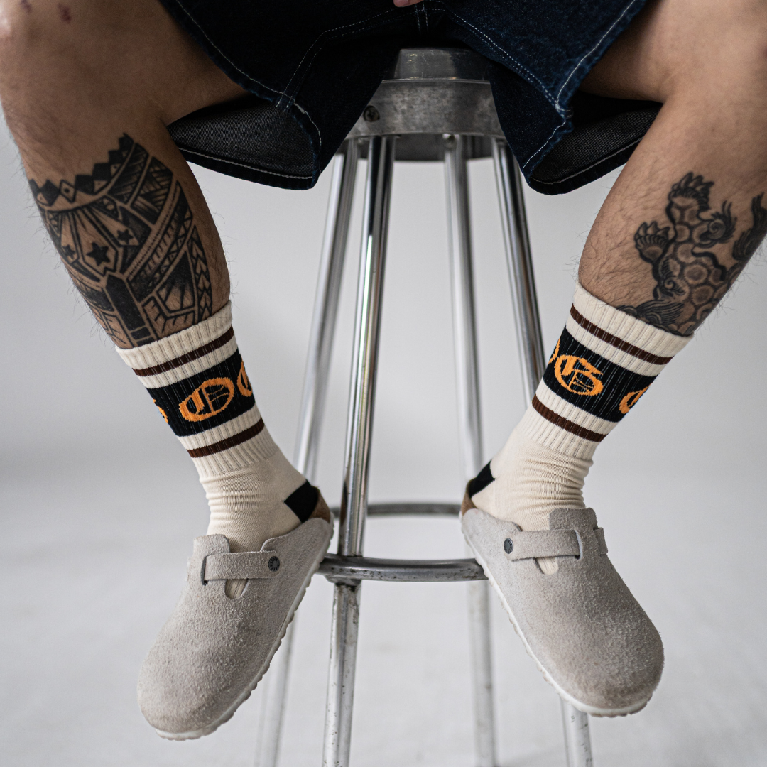 White OG socks with two espresso stripes and a black band with an orange OG logo worn by tattooed model
