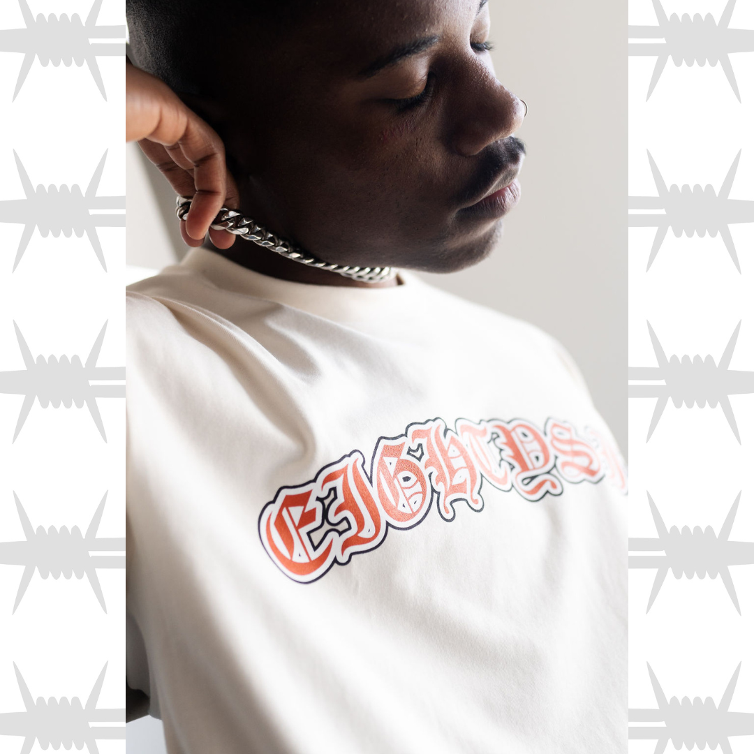 Old english script t-shirt in white with orange eightysix logo written in old english tattoo font, worn by a tattooed alternative model