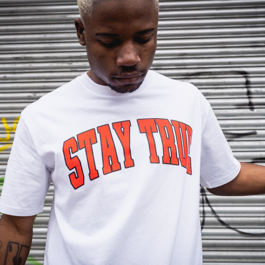 Stay true varsity graphic tee in white with orange stay true worn by tattooed alternative lifestyle model