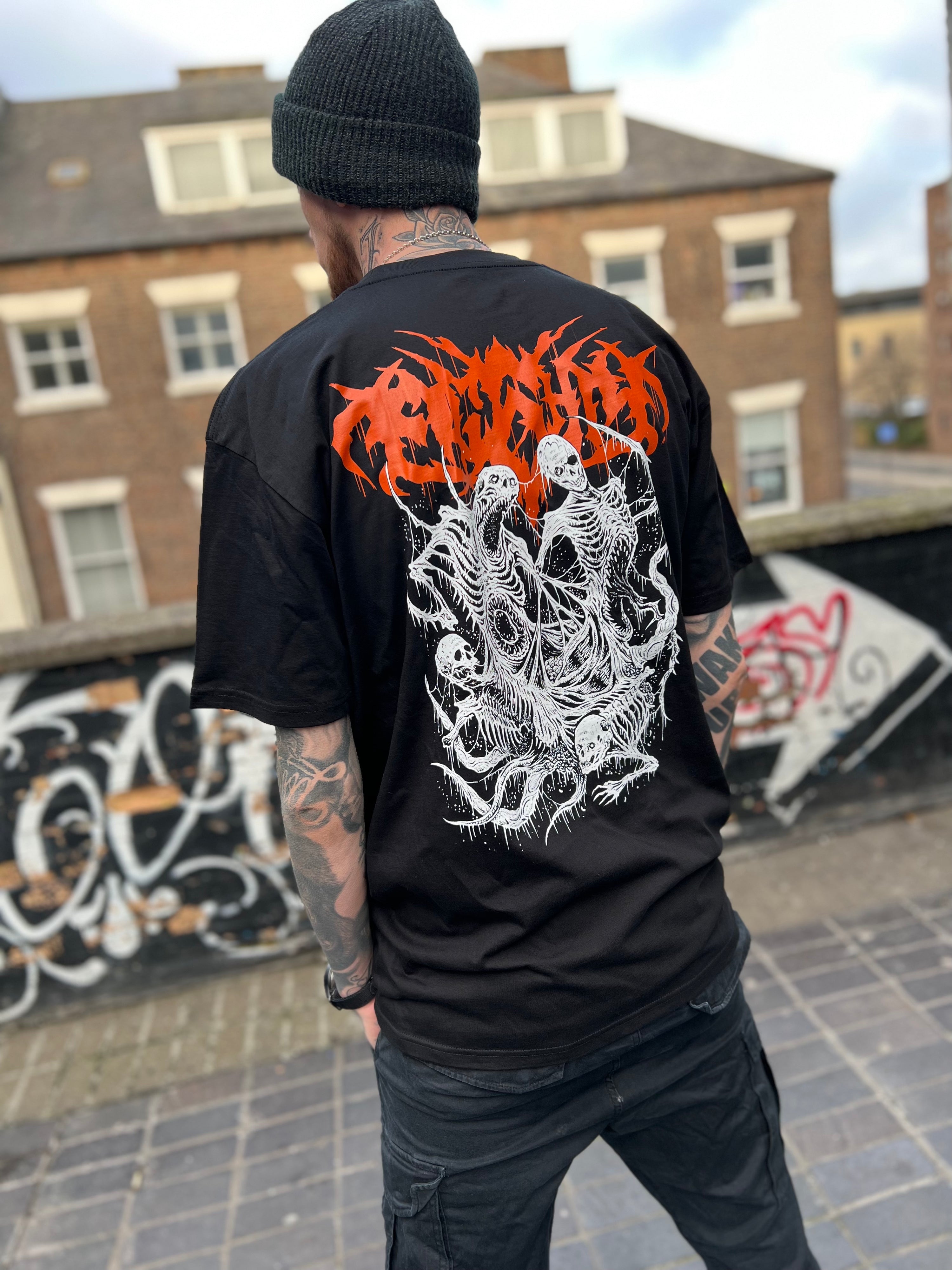 Death metal t-shirt worn by a tattooed model showing off the back visuals. The design is based around four tormented demons in a white print and the grunge script Eightysix logo in orange
