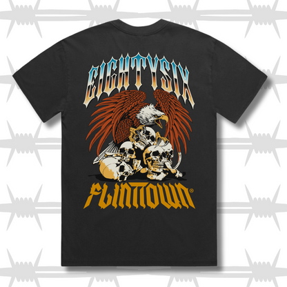 Eightysix X Flinttown t-shirt rear shot, shows eightysixlogo in a chrome tattoo style with an eagle protecting skulls in a tattoo style then the flinttown logo in orange below it.