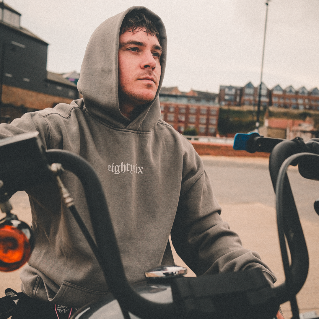 Model wearing grey hoodie with eightysix in white on front and tattoo inspired reaper design in the style of a king playing card