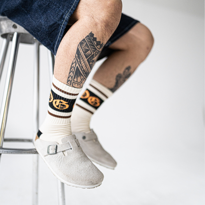 White OG socks with two espresso stripes and a black band with an orange OG logo worn by a tattooed model