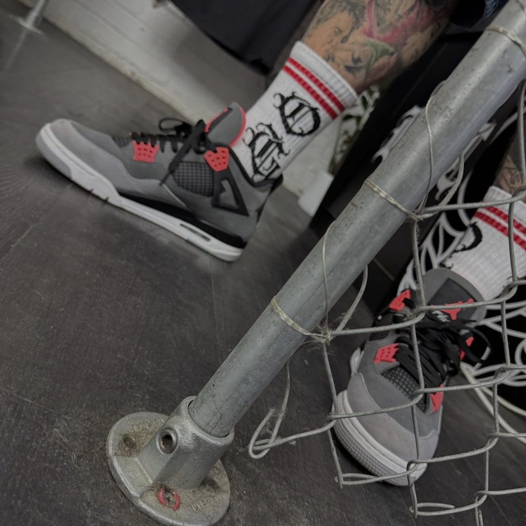 White OG socks with OG writen in old english and two red stripes worn by tattooed streetwear model