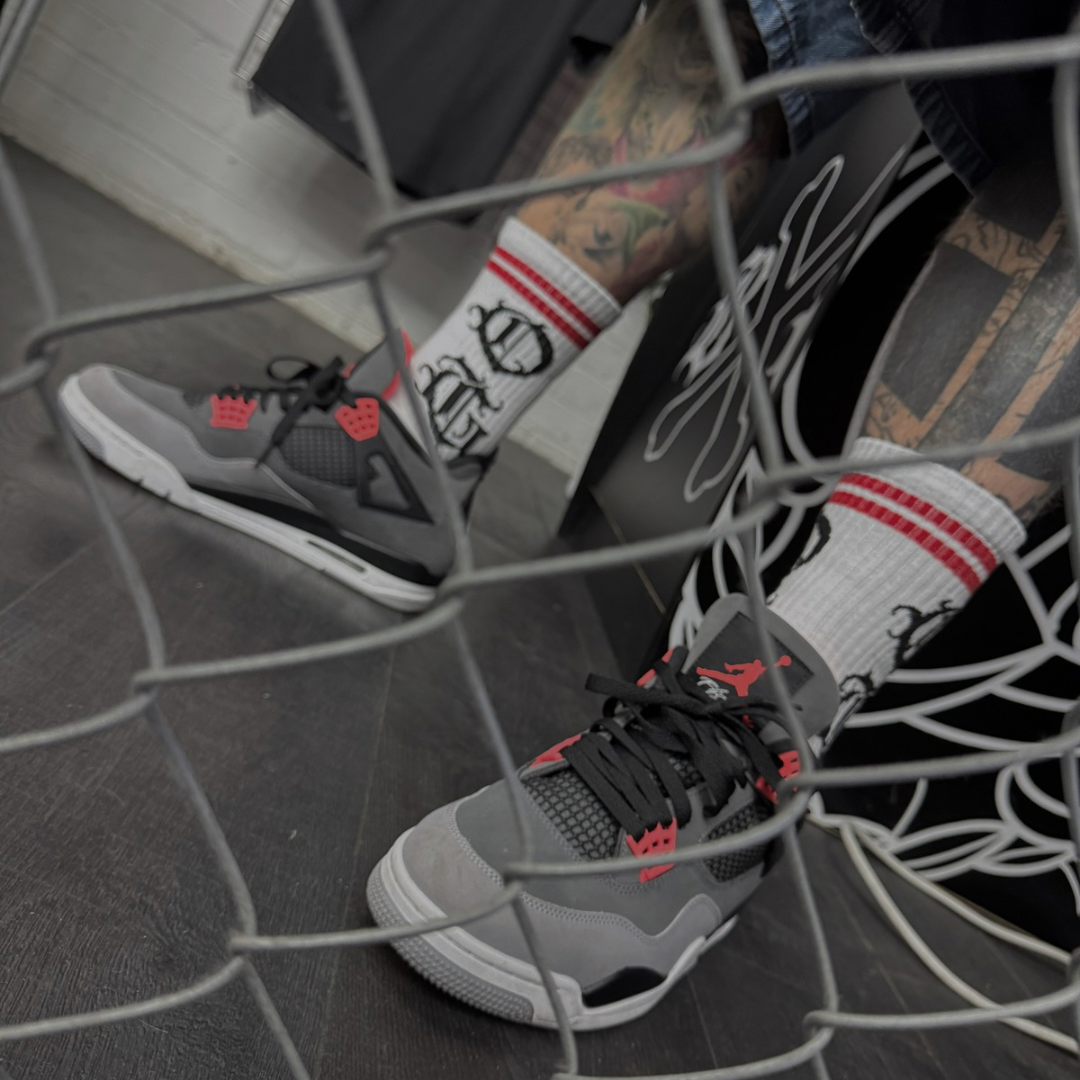 White OG socks with OG writen in old english and two red stripes worn by tattooed alternative model