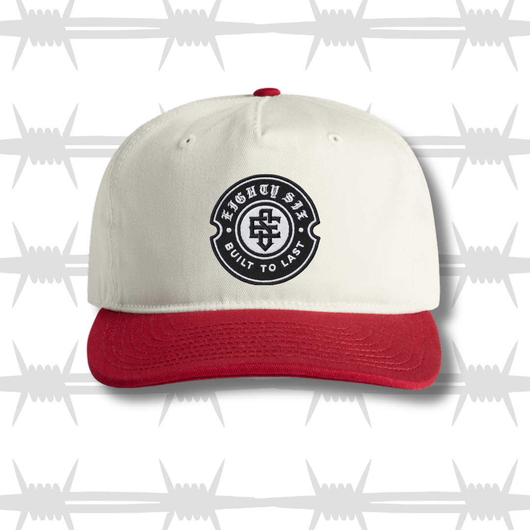 White and red two tone cap with black embroidered tattoo inspired skull and dagger design and built to last crest logo